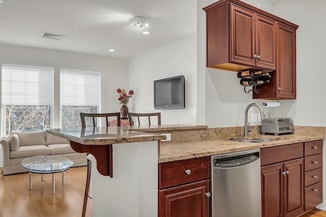 kitchen with a breakfast bar, dishwasher, sink, light stone counters, and kitchen peninsula