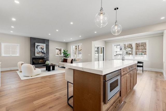 kitchen featuring stainless steel microwave, a center island, recessed lighting, light wood-style floors, and hanging light fixtures