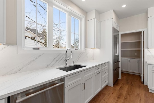 kitchen featuring light stone counters, a sink, white cabinets, appliances with stainless steel finishes, and backsplash