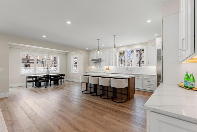 kitchen featuring backsplash, under cabinet range hood, high end refrigerator, light wood-style flooring, and white cabinets