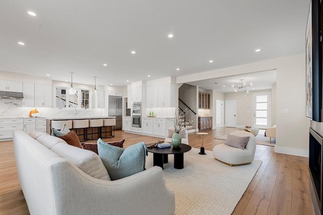 living room with stairway, baseboards, an inviting chandelier, recessed lighting, and light wood-type flooring