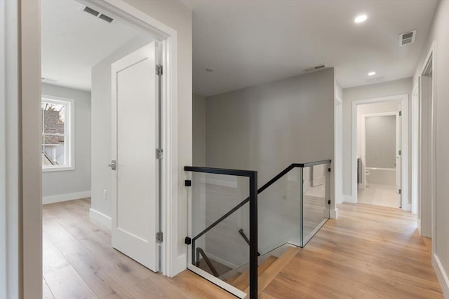 hall featuring an upstairs landing, visible vents, and light wood-type flooring