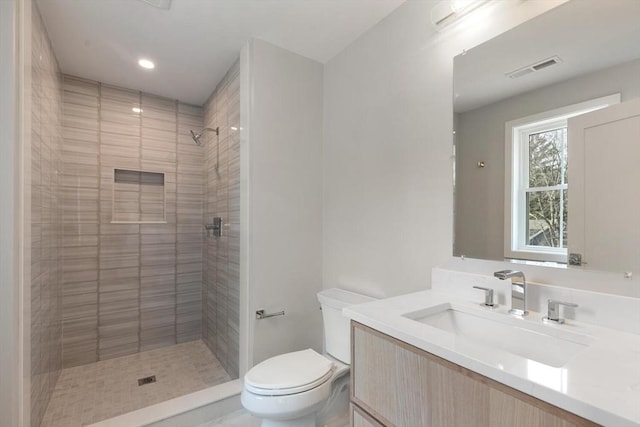 full bathroom with vanity, toilet, visible vents, and tiled shower