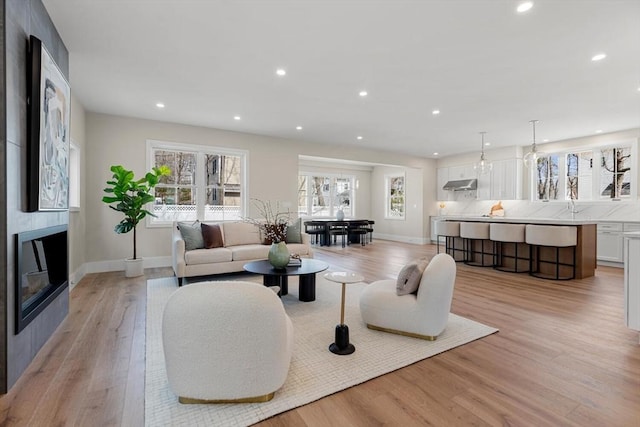 living area with a glass covered fireplace, baseboards, light wood-style flooring, and recessed lighting