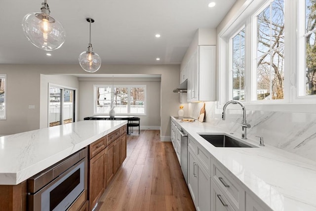 kitchen with light stone countertops, ventilation hood, stainless steel appliances, and a sink