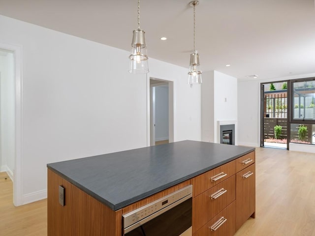 kitchen featuring light wood-type flooring, a center island, decorative light fixtures, and stainless steel oven