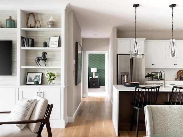 kitchen featuring hanging light fixtures, light hardwood / wood-style floors, white cabinets, decorative backsplash, and high end refrigerator