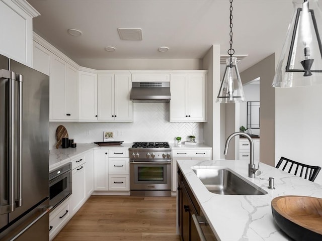 kitchen with sink, a breakfast bar area, light stone counters, decorative light fixtures, and premium appliances