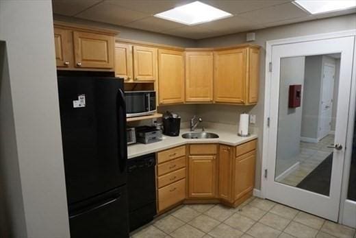 kitchen with black appliances, light brown cabinetry, a sink, and light countertops