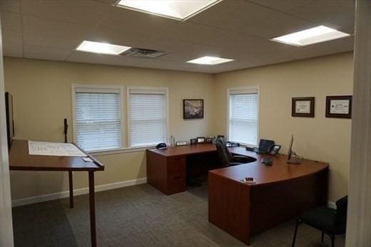 carpeted office space featuring visible vents, a paneled ceiling, and baseboards