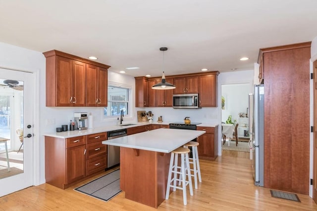 kitchen with stainless steel appliances, a sink, light wood-type flooring, a center island, and a kitchen bar