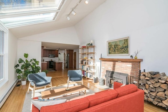 living area featuring baseboard heating, light wood-type flooring, a brick fireplace, high vaulted ceiling, and track lighting