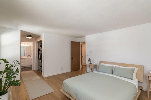 bedroom featuring light wood-style floors, baseboards, and ensuite bathroom