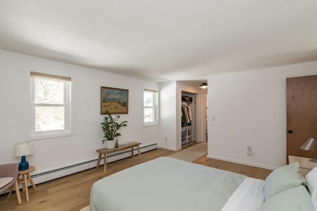 bedroom featuring light wood-style floors, baseboards, multiple windows, and a baseboard heating unit