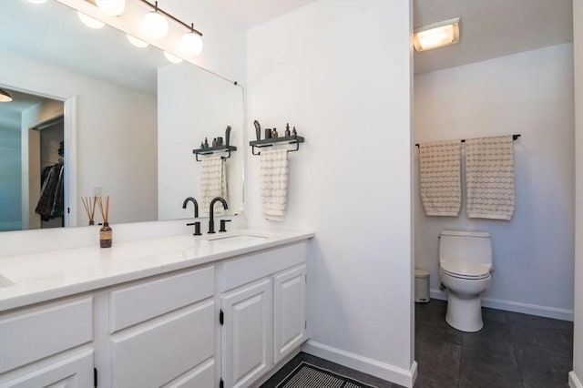 bathroom with double vanity, a sink, toilet, and baseboards