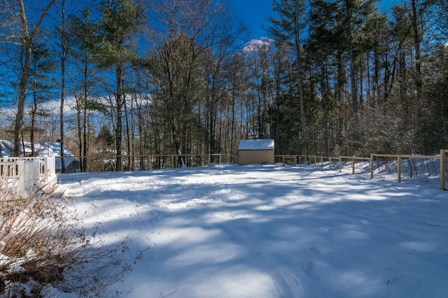 snowy yard with a storage shed, fence, a view of trees, and an outbuilding