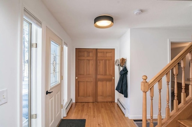 foyer entrance with a baseboard radiator, stairway, light wood-style flooring, and baseboards