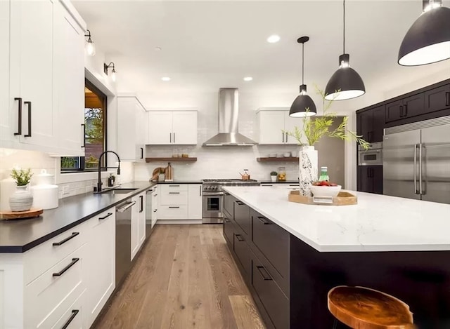 kitchen featuring backsplash, wall chimney exhaust hood, hanging light fixtures, light hardwood / wood-style floors, and high end appliances