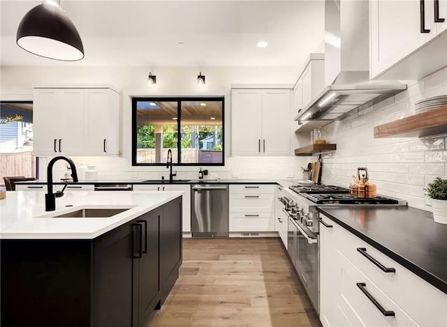 kitchen featuring wall chimney exhaust hood, decorative backsplash, appliances with stainless steel finishes, and light hardwood / wood-style floors