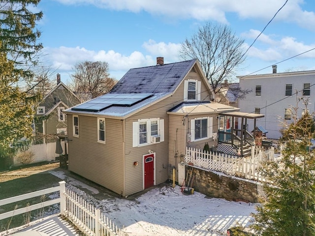 snow covered back of property featuring solar panels