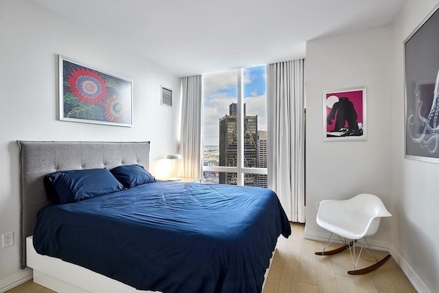 bedroom with a view of city, visible vents, expansive windows, wood finished floors, and baseboards