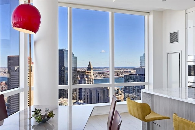 dining space featuring a water view, wood finished floors, visible vents, floor to ceiling windows, and a view of city