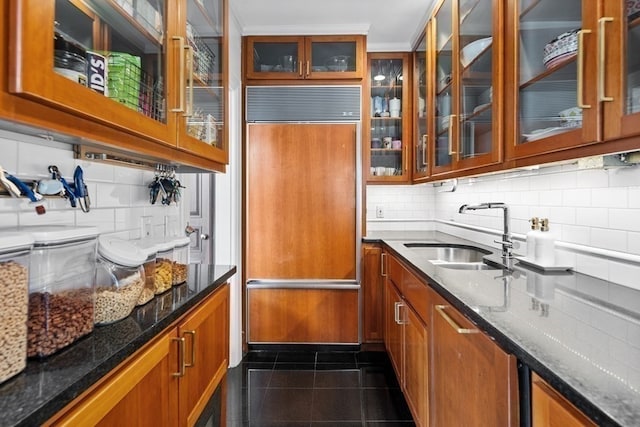 kitchen featuring dark stone counters, backsplash, dark tile patterned floors, sink, and paneled fridge