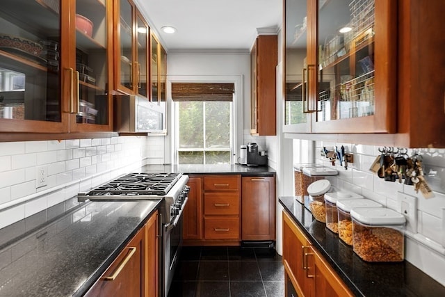 kitchen with high end stainless steel range oven, backsplash, dark tile patterned flooring, crown molding, and dark stone countertops