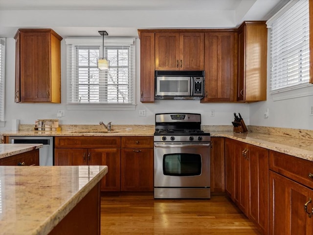 kitchen featuring light wood-style flooring, light stone countertops, appliances with stainless steel finishes, and a sink