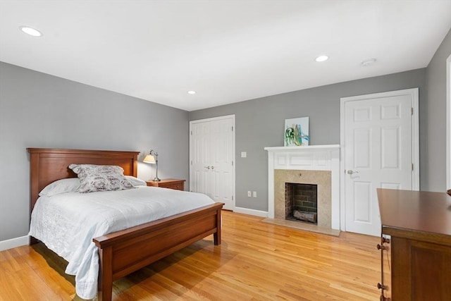 bedroom with light wood finished floors, recessed lighting, baseboards, a fireplace with flush hearth, and a closet