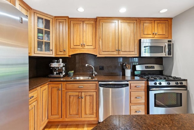 kitchen with a sink, decorative backsplash, stainless steel appliances, and dark stone countertops