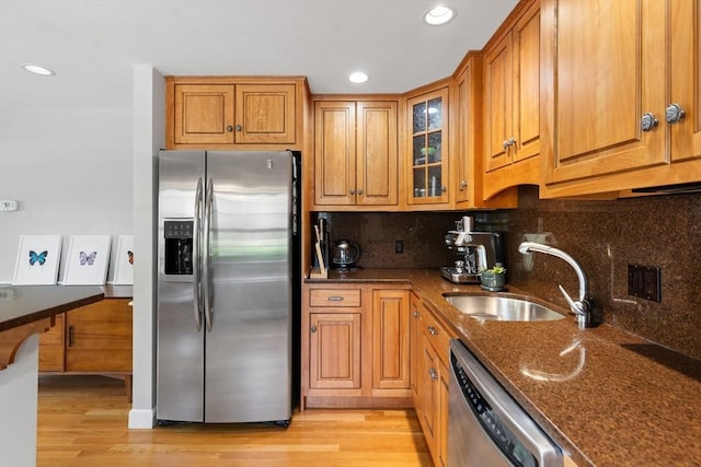 kitchen with brown cabinets, appliances with stainless steel finishes, a sink, light wood-style floors, and glass insert cabinets