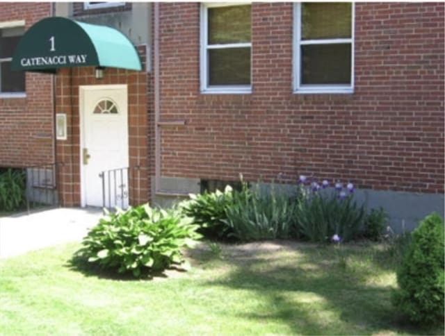 doorway to property featuring a yard and brick siding