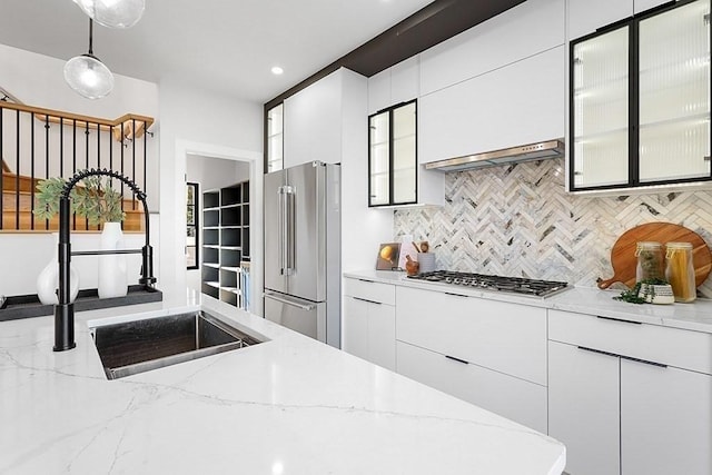 kitchen featuring stainless steel appliances, a sink, range hood, backsplash, and pendant lighting