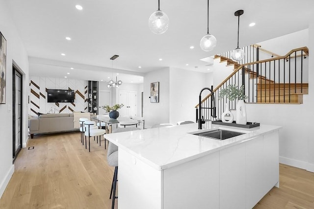 kitchen with light wood finished floors, recessed lighting, a kitchen island with sink, modern cabinets, and a chandelier