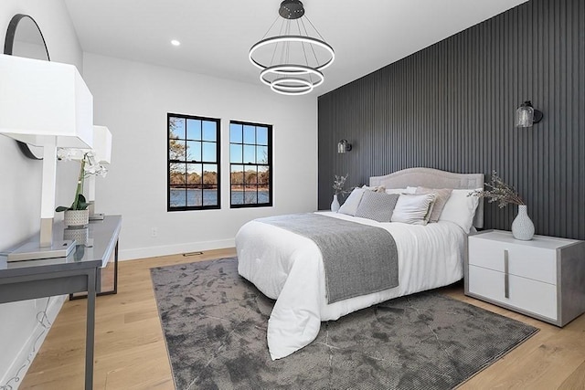 bedroom featuring a chandelier, an accent wall, light wood-type flooring, baseboards, and recessed lighting