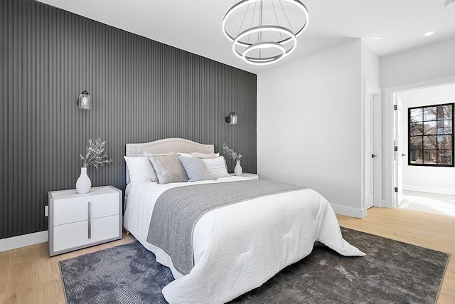 bedroom with wood finished floors, a chandelier, an accent wall, baseboards, and recessed lighting