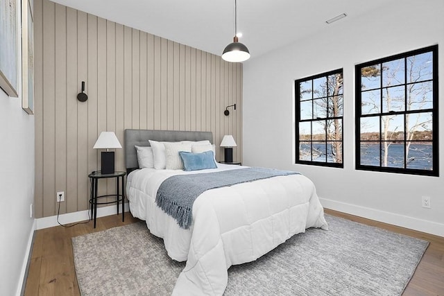 bedroom featuring wood finished floors, baseboards, and wooden walls