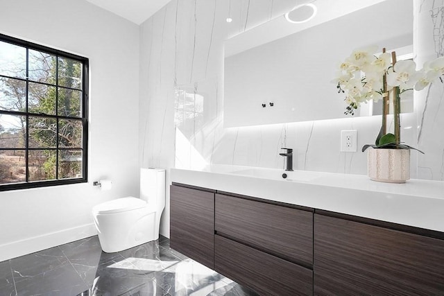 bathroom with marble tiled floors, healthy amount of natural light, vanity, and toilet