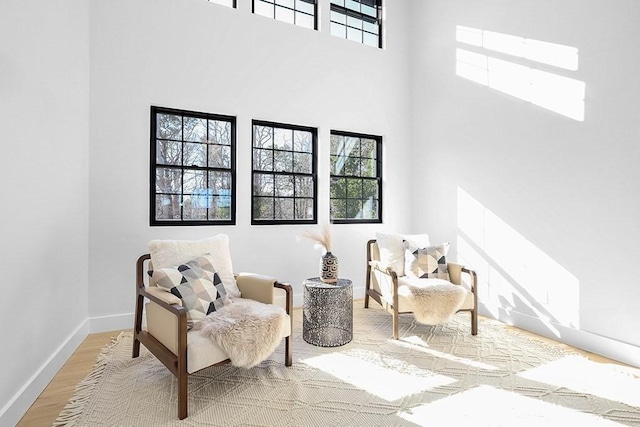living area with plenty of natural light, wood finished floors, baseboards, and a towering ceiling