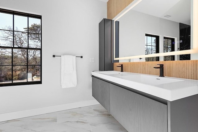 full bathroom featuring marble finish floors, baseboards, plenty of natural light, and double vanity
