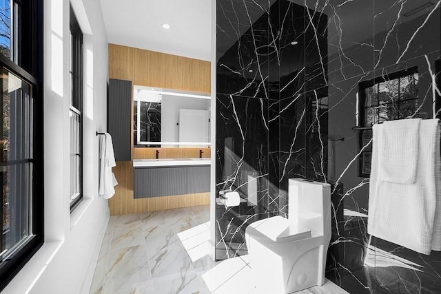 full bath featuring marble tiled flooring, recessed lighting, toilet, double vanity, and stone wall