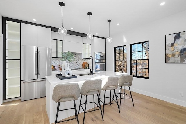 kitchen featuring freestanding refrigerator, modern cabinets, light countertops, a center island with sink, and recessed lighting