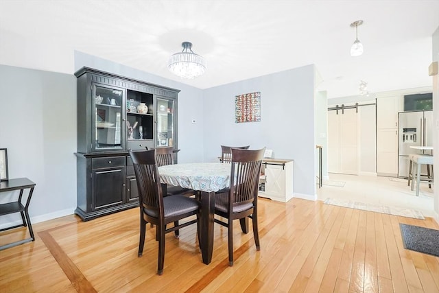 dining area with light wood-type flooring, baseboards, and a barn door