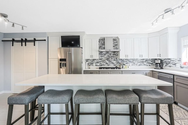 kitchen with track lighting, wall chimney exhaust hood, decorative backsplash, and stainless steel appliances
