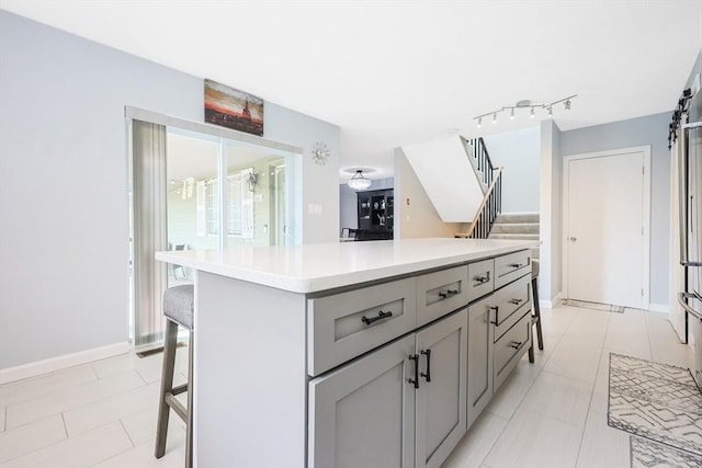 kitchen featuring a barn door, gray cabinetry, light countertops, a kitchen island, and a breakfast bar area