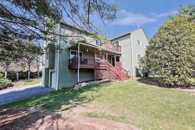 back of house featuring driveway, a wooden deck, an attached garage, a lawn, and stairs
