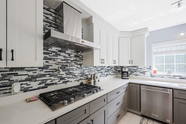 kitchen featuring gray cabinets, wall chimney range hood, decorative backsplash, and appliances with stainless steel finishes