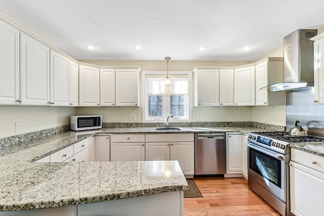 kitchen featuring sink, decorative light fixtures, appliances with stainless steel finishes, wall chimney range hood, and white cabinets