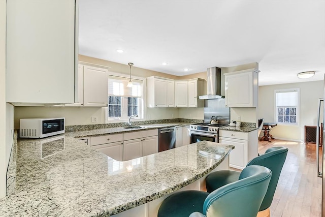 kitchen featuring pendant lighting, wall chimney range hood, stainless steel appliances, light stone countertops, and kitchen peninsula